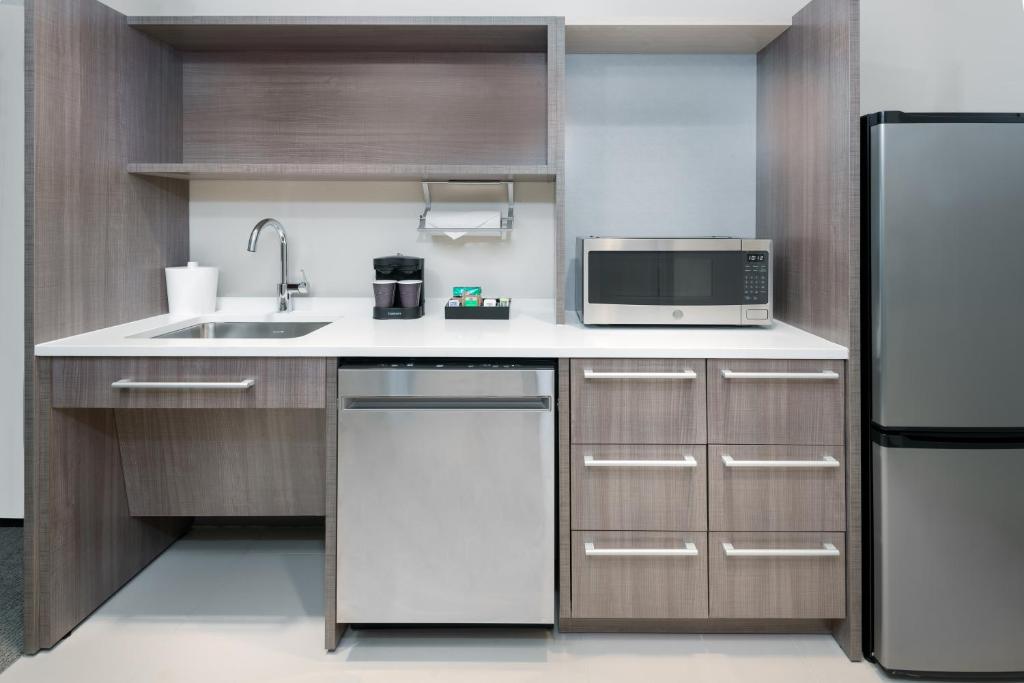 cozinha equipada com armários em tons de madeira clara, fogão, pia com espaço para cadeira de rodas, micro-ondas e forno no Home2 Suites By Hilton Orlando Near Universal, um dos hotéis com cozinha em Orlando