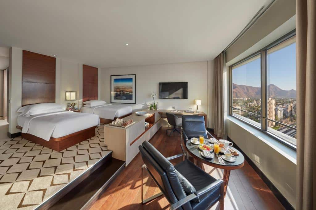 Quarto do Mandarin Oriental, com duas camas de casal do lado esquerdo e do lado direito do quarto duas poltronas com uma mesa redonda em frente às janelas.