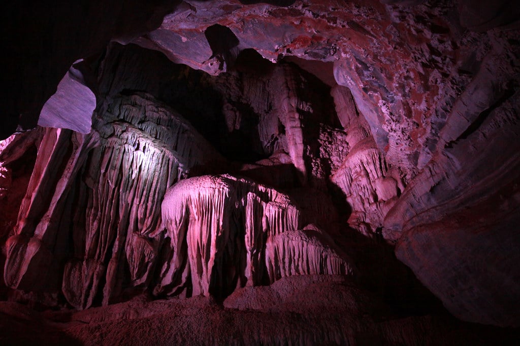 Interior da Gruta da Lapinha em Lagoa Santa. Ela está iluminada por uma luz roxa e é possível ver diversas formações pontiagudas.