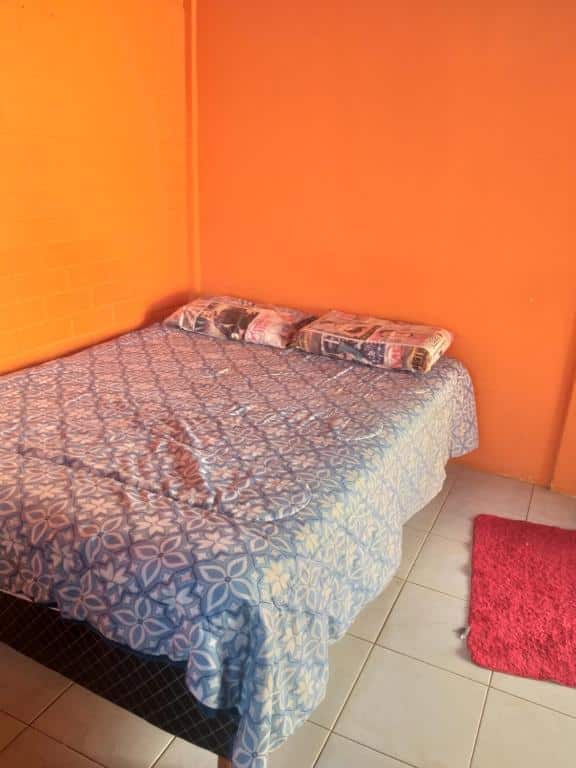 Quarto das acomodações koynonya. As paredes são laranjas, há uma cama box de casal encostada na parede esquerda, e também há um pequeno tapete vermelho na direita.
