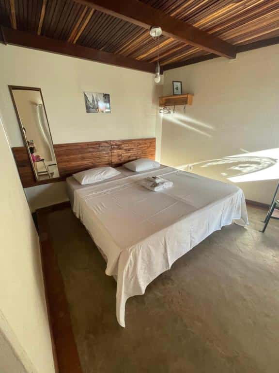 Foto do quarto da Kitnet Apart Hotel 2, que representa o post sobre hotéis e pousadas em Sete Lagoas. No centro há uma cama box de casal com toalhas em cima. À sua esquerda, tem um espelho, e na direita, uma prateleira de madeira com cabides.