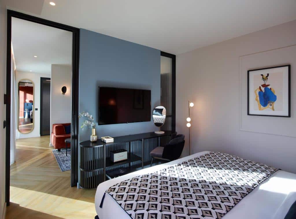 Quarto moderno no Say Hotel com colcha estampada, TV na parede, escrivaninha e arte na parede, conectado a uma área de estar, para representar hotéis em Atenas.