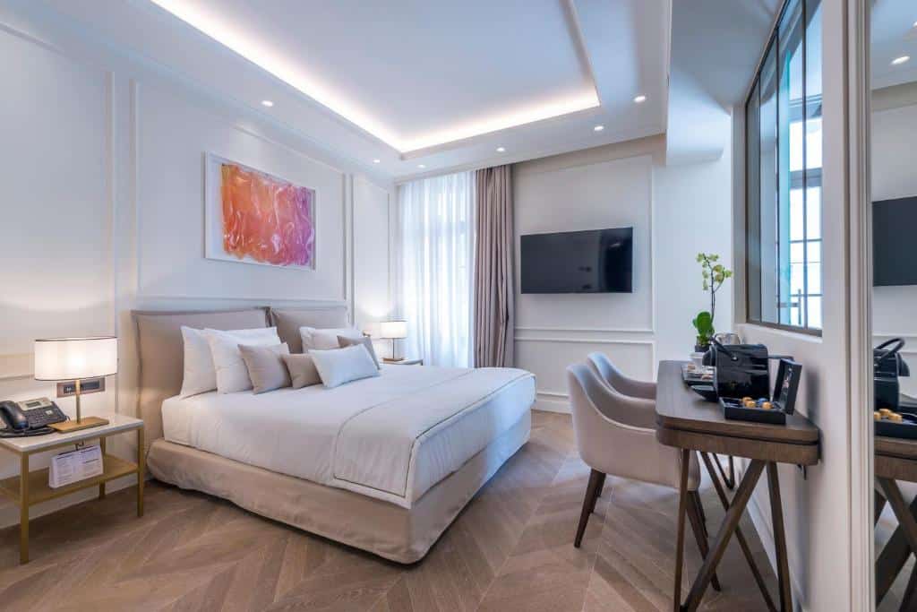 Quarto moderno no The Residence Aiolou Suites & SPA com uma cama grande, escrivaninha, TV na parede, obras de arte abstratas e duas luminárias de cabeceira, para representar hotéis em Atenas.