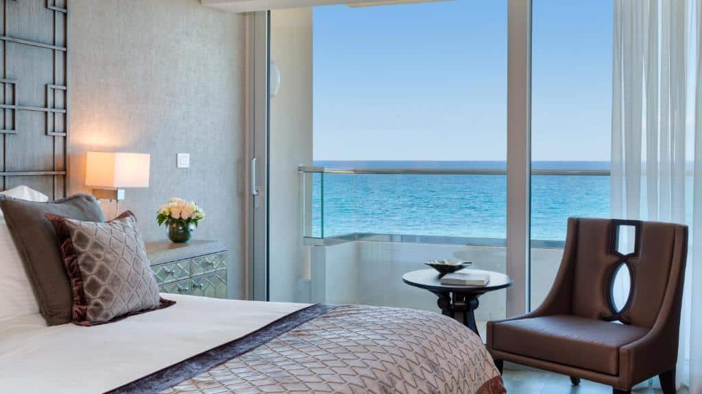 Um quarto moderno no Divani Apollon Palace & Thalasso com uma cama, poltrona, mesa e uma varanda com vista para o oceano sob um céu claro, para representar hotéis em Atenas.