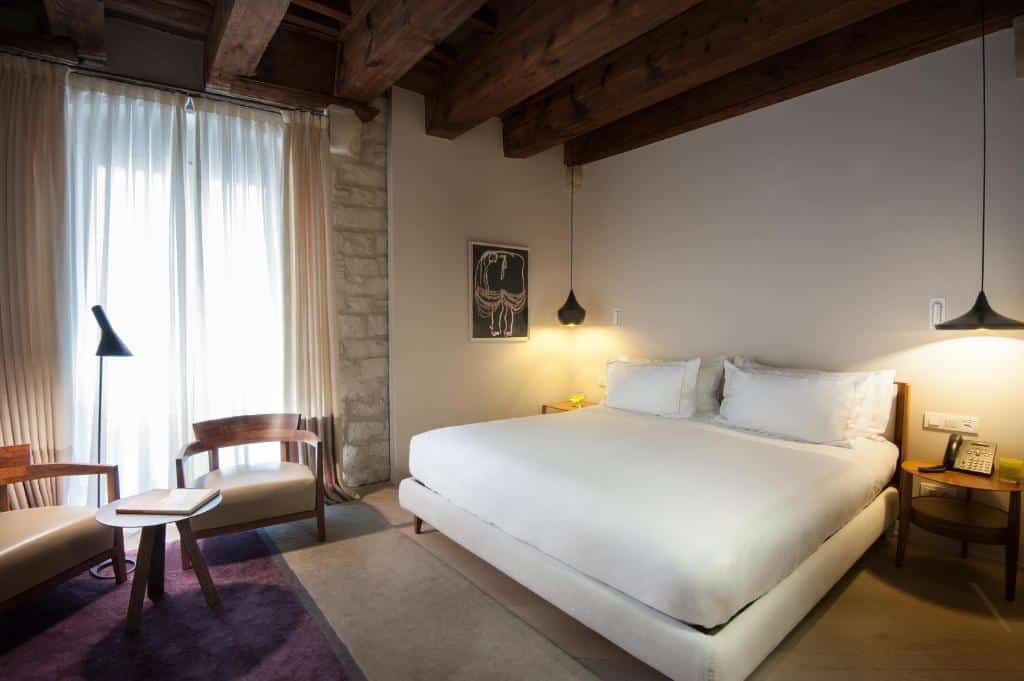 Quarto do Mercer Hotel. Há mesinhas de cabeceira com abajures pendurados dos dois lados da cama de casal. Há uma janela na parede ao lado, e duas cadeiras estão na sua frente. Uma mesinha de centro e uma luminária estão próximas às cadeiras.