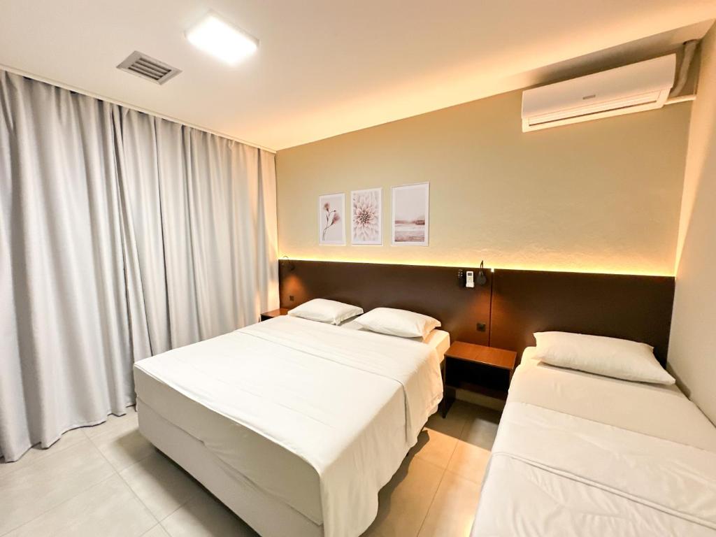Um quarto do Presto Hotel com uma cama de casal e uma cama de solteiro, paredes bege, três obras de arte na parede e cortinas fechadas, para representar hotéis em Blumenau.