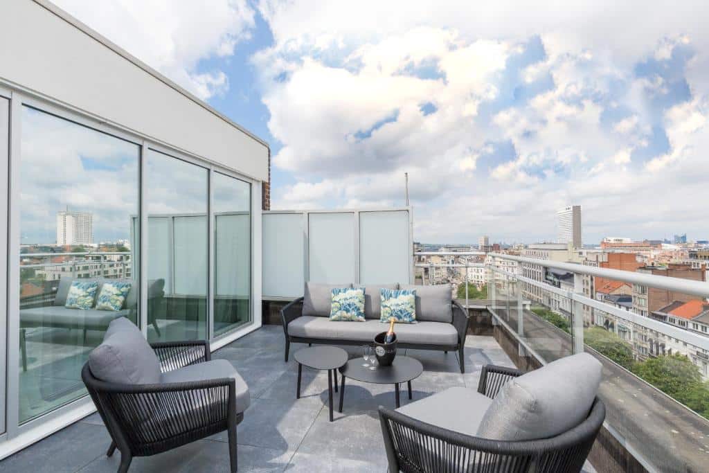 varanda a céu aberto do Thon Hotel Bristol Stephanie, um dos hotéis em Bruxelas, com duas poltronas e um sofá em cinza, com porta de vidro e muitas nuvens acima