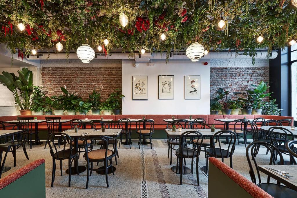 lounge com mesinhas e cadeiras no Urban Yard Hotel, um dos hotéis em Bruxelas, com luminárias penduradas junto com um teto arborizado