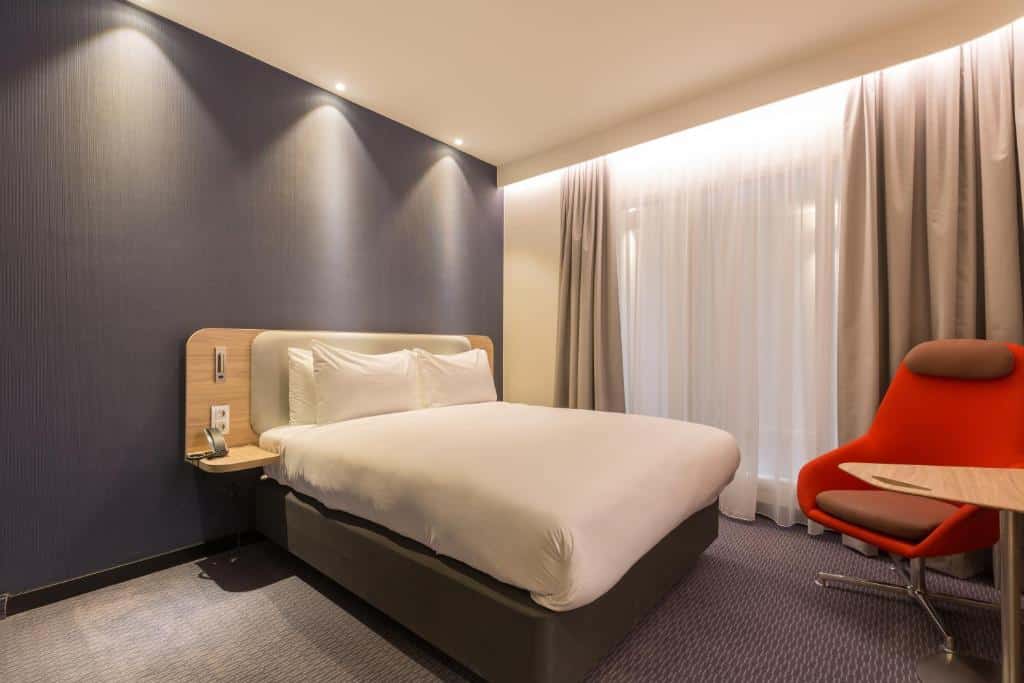 quarto amplo do Holiday Inn Express Brussels-Grand-Place, um dos hotéis em Bruxelas, com cama de casal queen e janela grande com cortina, há ainda uma poltrona e mesa