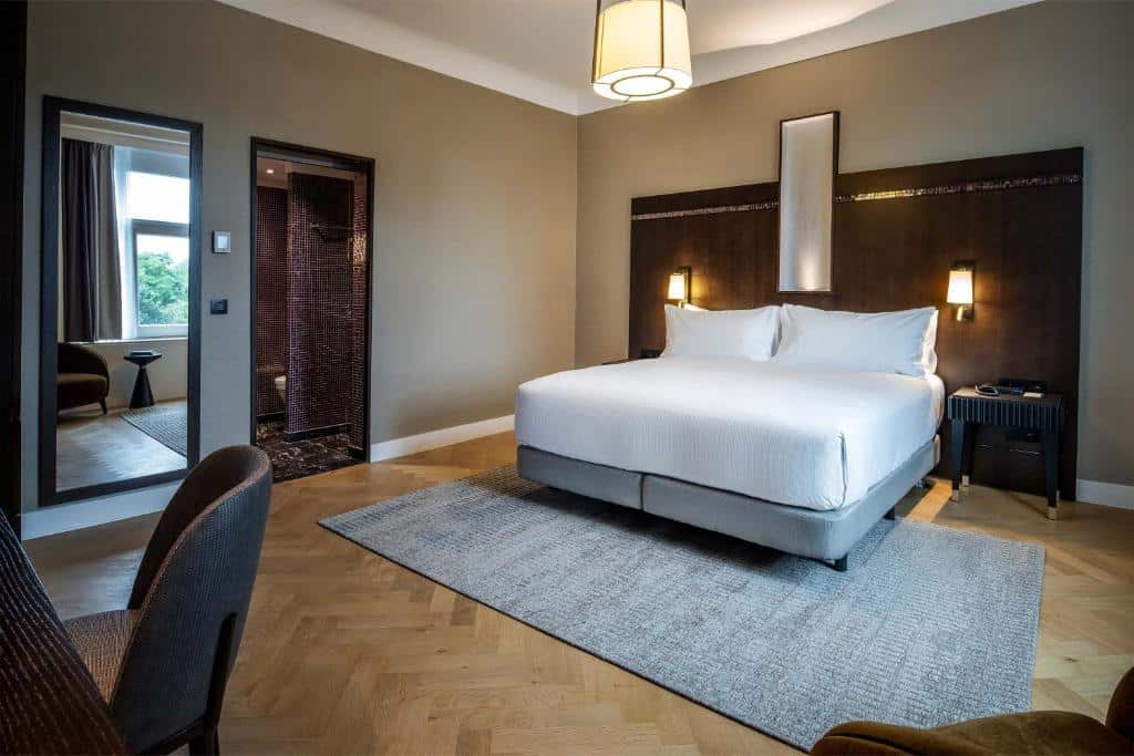 quarto com bastante espaço no DoubleTree By Hilton Brussels City, um dos hotéis em Bruxelas, com cama de casal, mesa com poltrona, luminária de teto e também ao lado das camas