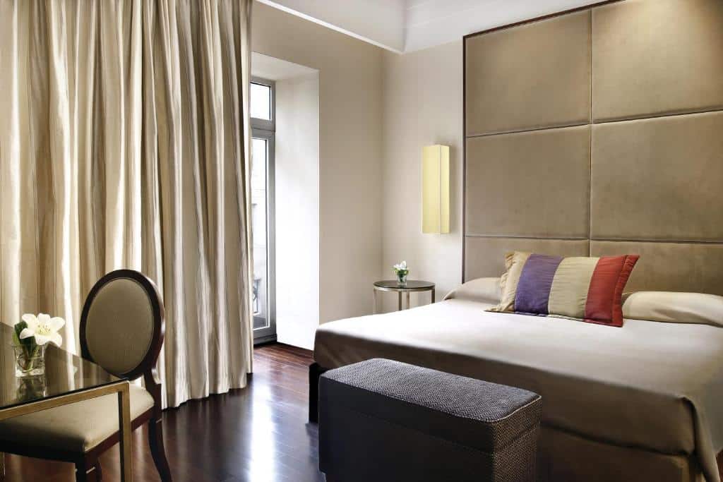 Quarto do Savoy Hotel com uma cama de casal, uma mesinha de escritório com uma cadeira, e uma sacada, o chão é de madeira e a decoração é em tons de bege e cinza, para representar hotéis em Buenos Aires.