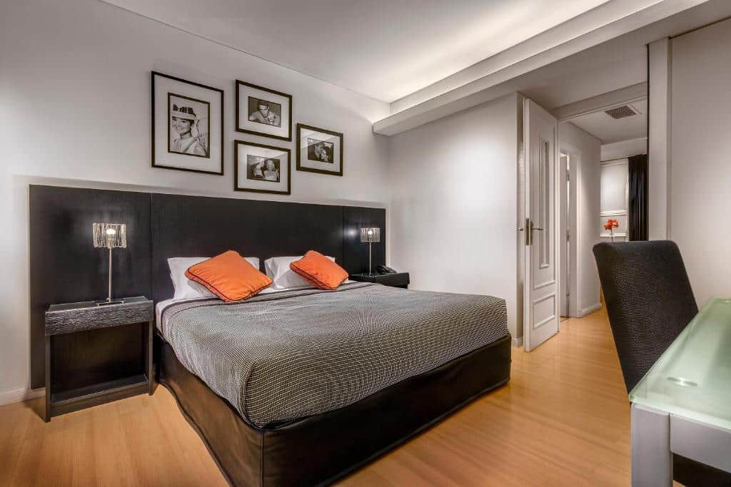 Quarto do Broadway Hotel & Suites em Buenos Aires que é bastante amplo com quadros na parede e mesinha e luminária de ambos os lados da cama, há uma porta para o banheiro e mais móveis em frente.
