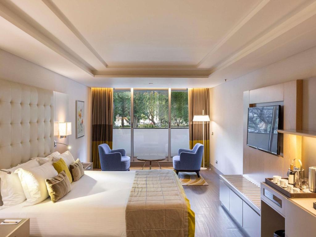 Um quarto moderno no Palladio Hotel Buenos Aires - MGallery com uma cama grande, duas cadeiras azuis perto de uma janela, uma TV e uma cafeteria, para representar hotéis em Buenos Aires.