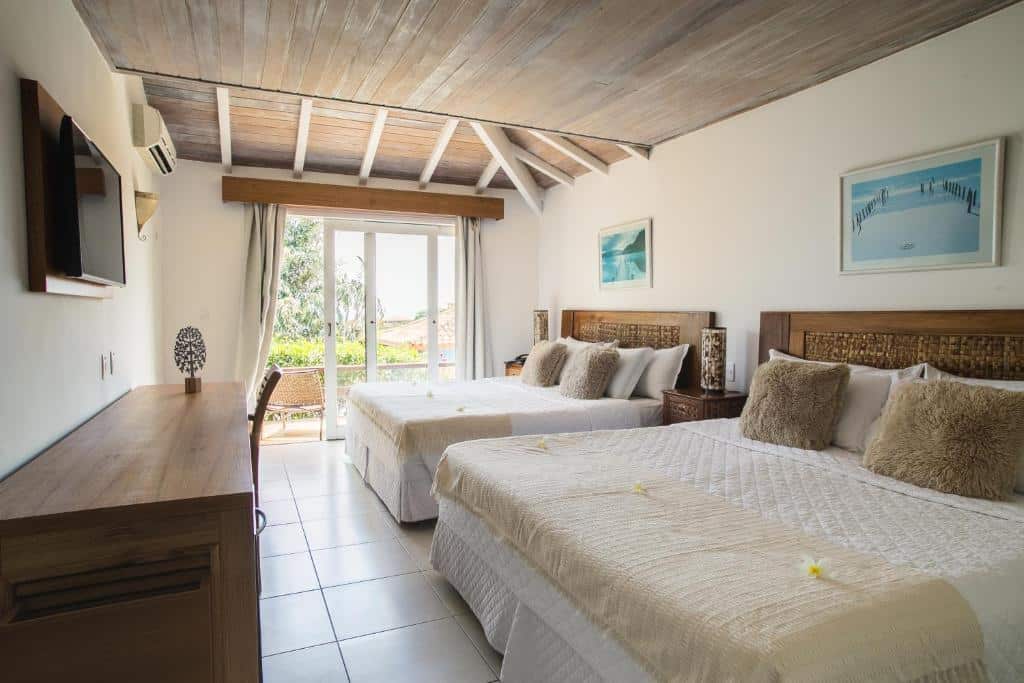 Um quarto na La Pedrera Small Hotel & Spa na Praia João Fernandes, com duas camas de casal, uma TV, uma escrivaninha e uma varanda com vista para as palmeiras do lado de fora, para representar hotéis em Búzios.