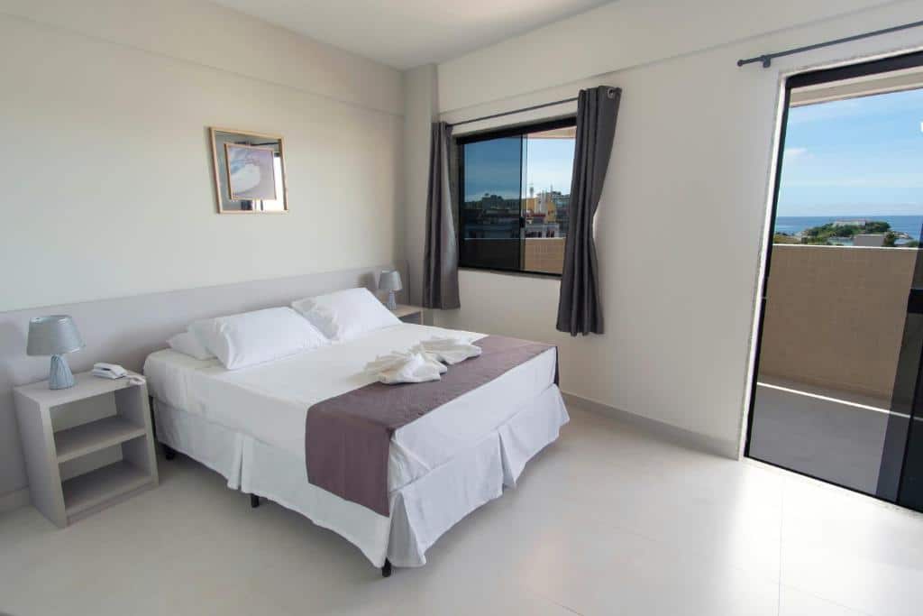 Quarto simples no Hotel Mirante do Forte com paredes brancas, cama de casal e varanda com vista para o mar, para representar hotéis em Cabo Frio.