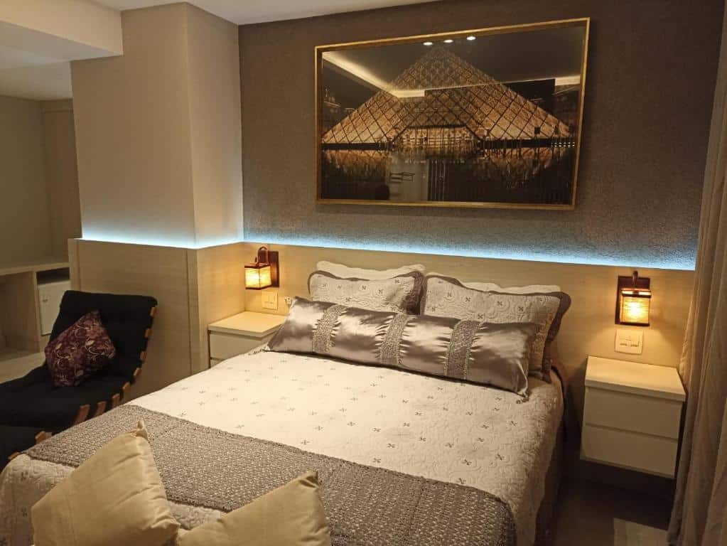 Quarto na Nova Onda Hotel com uma cama de casal com uma luz de led na cabeceira e quadro do museu do louvre em cima, para representar hotéis em Cabo Frio.