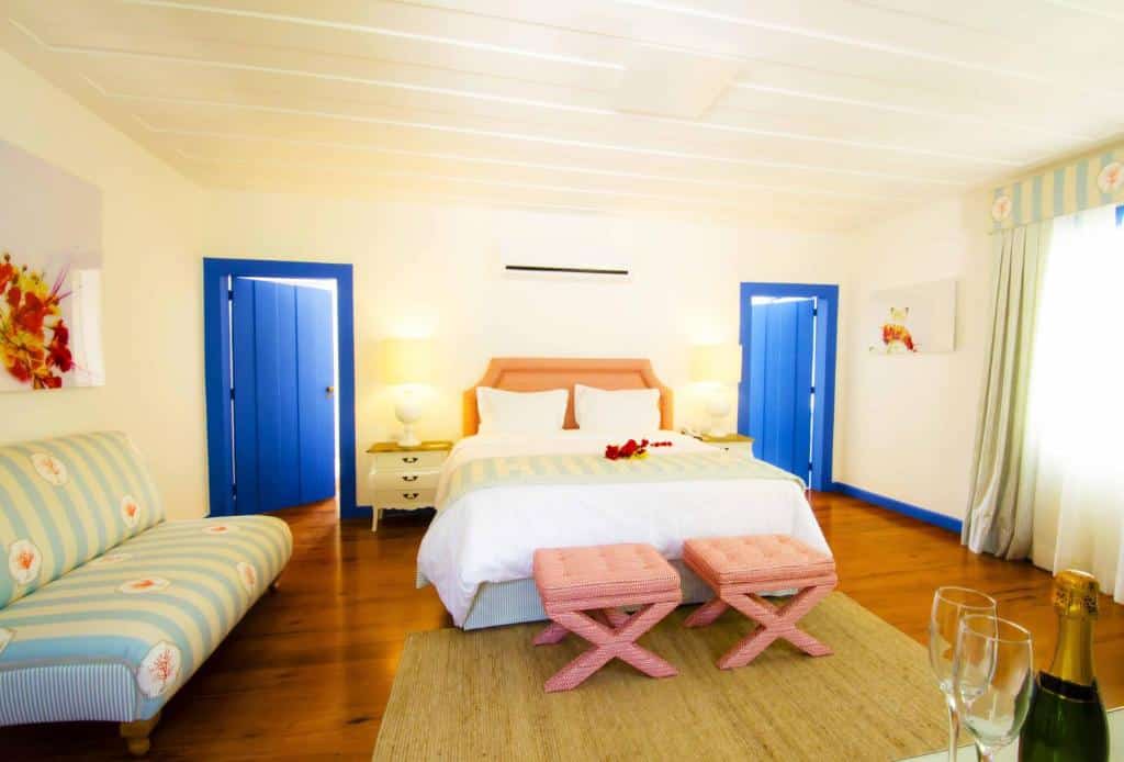 Quarto espaçoso no Hotel Solar do Arco com grande casa de casal, duas portas azuis, sofá e taças com champagne, para representar hotéis em Cabo Frio.