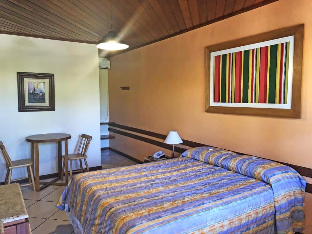 Quarto do Hotel Mar de Cabo Frio com uma parede laranja, outra parede branca, quadros decorativos e cama de casal, para representar hotéis em Cabo Frio.