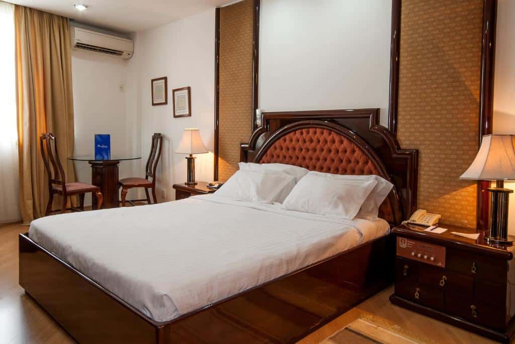 Um quarto do Américas Benidorm Hotel com uma cama de casal, mesas laterais, luminárias, duas cadeiras, uma mesa e um ar-condicionado na parede, para representar hotéis em Copacabana.