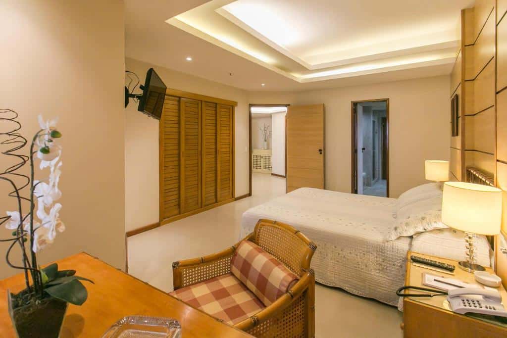 Um quarto no Mirador Rio Copacabana Hotel com uma cama de casal, escrivaninha, cadeira, TV na parede, armário e iluminação aconchegante, para representar hotéis em Copacabana.