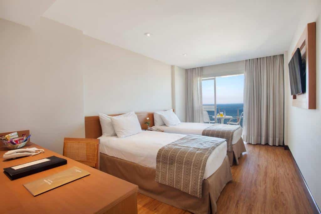 Quarto no Windsor Palace com duas camas de solteiro, uma escrivaninha, TV na parede e uma varanda com vista para o mar, para representar hotéis em Copacabana.