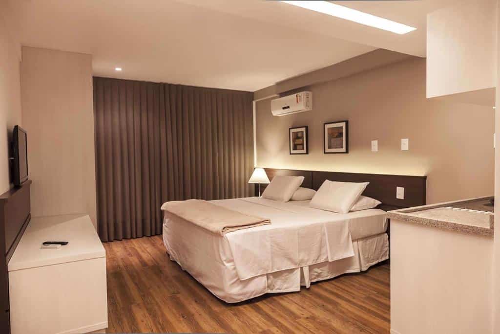 Um quarto do Atmosfera Hotel moderno com uma cama de casal, abajur, TV, ar-condicionado e cortinas fechadas.