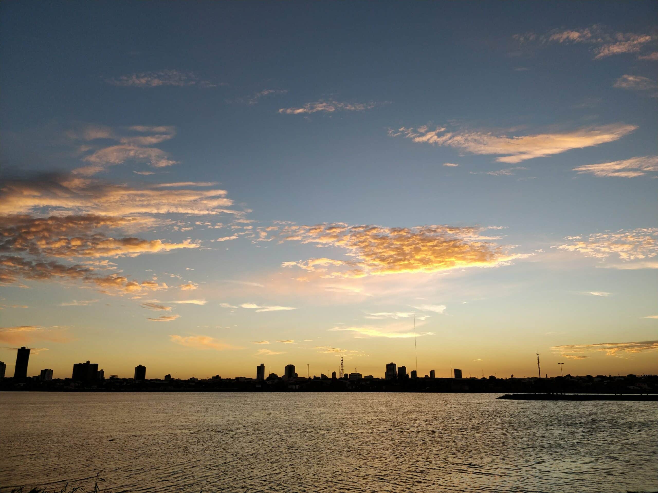 Silhueta do horizonte da cidade de Feira de Santana, Bahia ao pôr do sol com nuvens acima e água calma em primeiro plano.