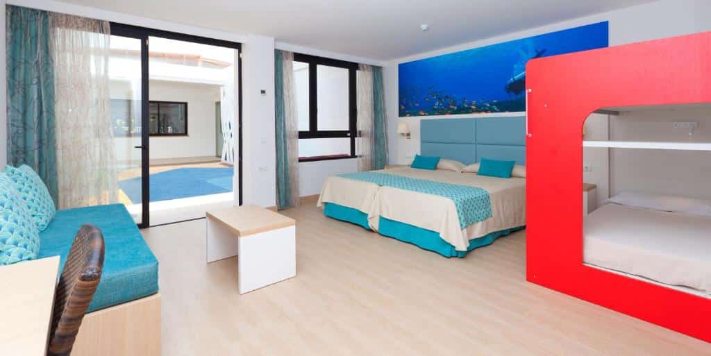 Quarto do Marvell Club Hotel & Apartments com duas camas, um beliche, um sofá, uma escrivaninha e janelas grandes com vista para a área da piscina.