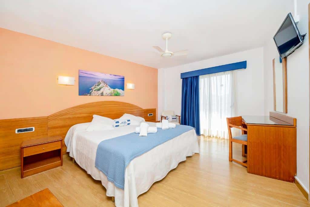 Quarto do Hostal Manolita bem iluminado com uma cama grande, escrivaninha, TV na parede e janela com cortinas que permitem a entrada de luz natural.
