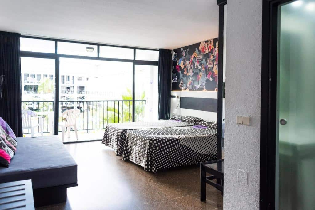 Quarto do Ibiza Rocks Hotel com duas camas, colchas de bolinhas, arte na parede, sofá, varanda e janelas grandes que permitem a entrada de luz natural.