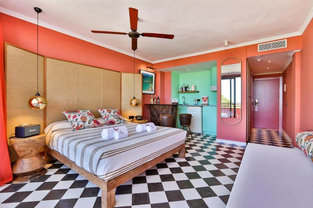 Quarto do Cubanito Ibiza colorido com cama de casal, ventilador de teto, área de bar e piso de ladrilho xadrez em preto e branco.