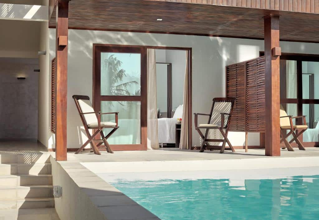 Duas cadeiras de madeira em um pátio ao lado de uma piscina, com portas de vidro deslizantes que levam a uma sala moderna.