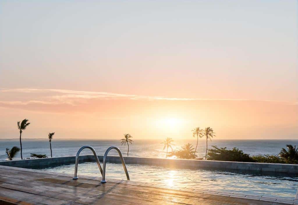 Piscina infinita com vista para o oceano e palmeiras, fotografada ao nascer ou pôr do sol sob um céu limpo. Este é um dos hotéis em Jericoacoara.