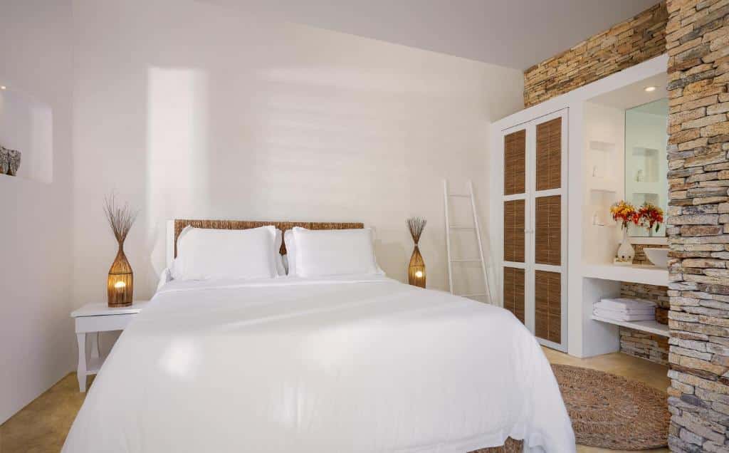Um quarto moderno com uma cama branca, detalhes em vime, parede de pedra, mesas de cabeceira e iluminação suave.