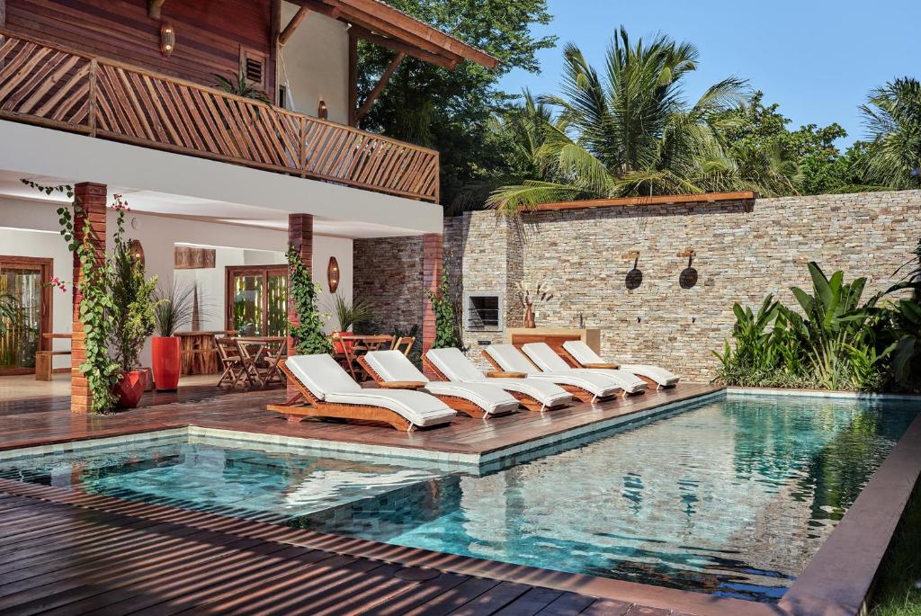 Piscina externa com cinco espreguiçadeiras, deck de madeira, parede de pedra e plantas tropicais ao lado de uma moderna casa de dois andares. Este é um dos hotéis em Jericoacoara.