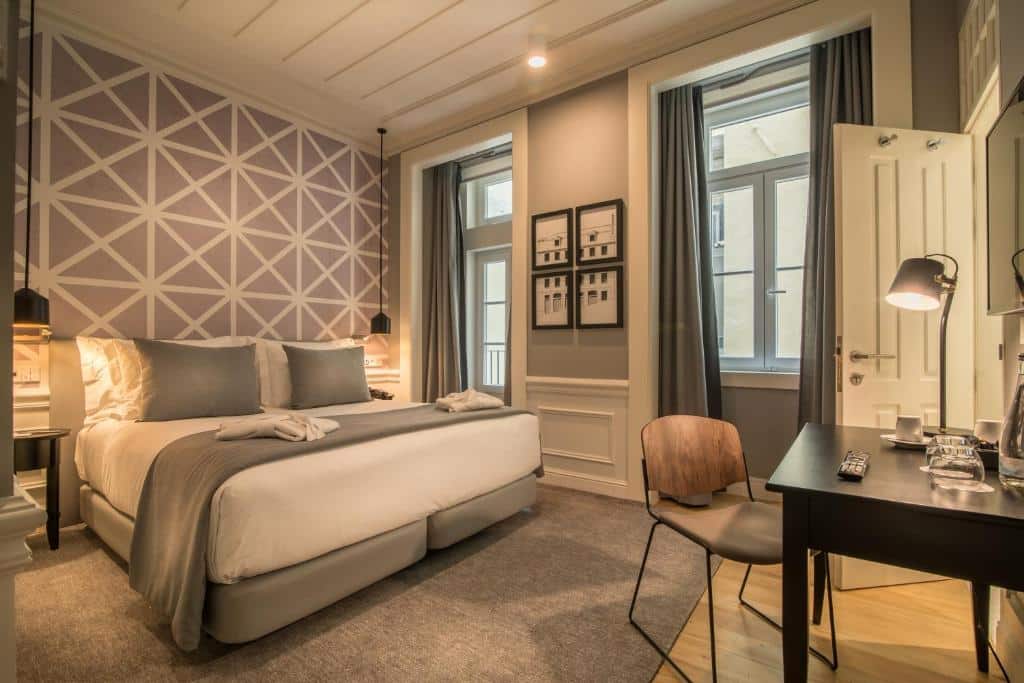 Quarto aconchegante no Hotel da Baixa, com cama box de casal, luminárias pendentes sobre as mesinhas de cabeceira, janelas com cortina blecaute, e mesa de trabalho com TV presa à parede logo acima, para representar hotéis em Lisboa.