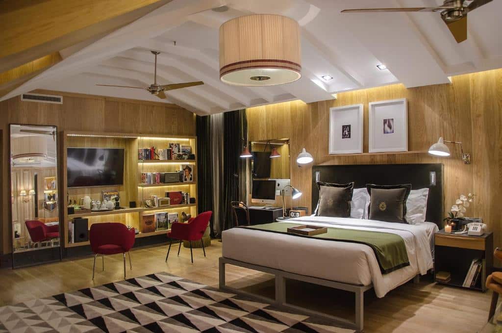 Quarto amplo, com cama de casal tamanho queen, espelho de corpo inteiro, ventiladores de teto, lustre, painel com TV e decorações, além de duas poltronas e uma mesinha de trabalho, no Browns Central Hotel, para representar hotéis em Lisboa.
