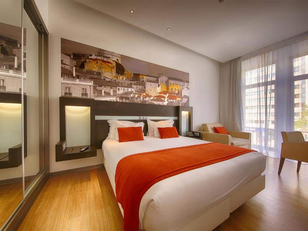 Quarto no Jupiter Lisboa Hotel, com cama ampla de casal, mesinha de cabeceira, quadro de Lisboa, poltrona e cortina voil na sacada, para representar hotéis em Lisboa.