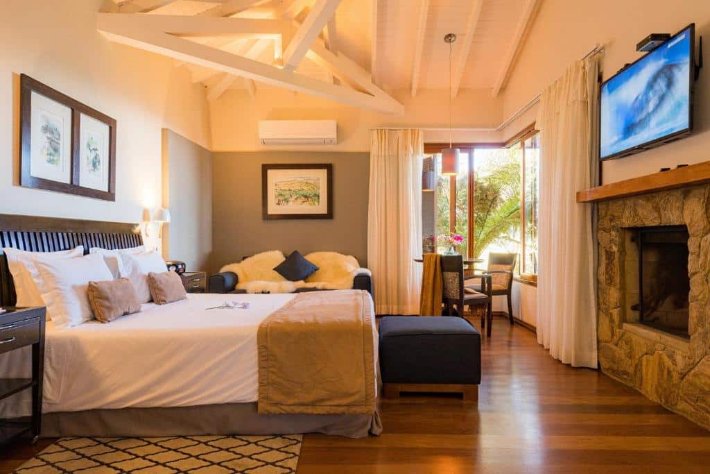Um quarto aconchegante no Kuriuwa Hotel com uma cama grande, piso de madeira, lareira, TV e janelas que permitem a entrada de luz natural, para representar hotéis em Monte Verde.