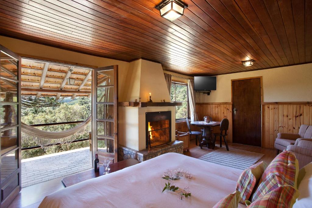 Quarto aconchegante com teto de madeira, lareira, cama, mesa e portas abertas que levam a uma rede em uma varanda com vista para a natureza, no Hotel Fazenda Itapuá, para representar hotéis em Monte Verde.
