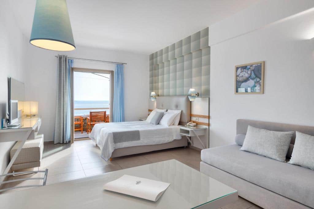 Quarto moderno no Lithos by Spyros & Flora com cama de casal, sofá, escrivaninha, TV e varanda com vista para o mar e assentos ao ar livre, para representar hotéis em Mykonos.