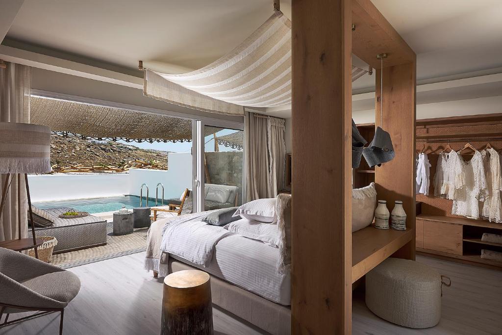 Quarto no Palladium Hotel com cama de dossel, armário aberto, área de estar e um terraço com uma pequena piscina e espreguiçadeiras do lado de fora, para representar hotéis em Mykonos.
