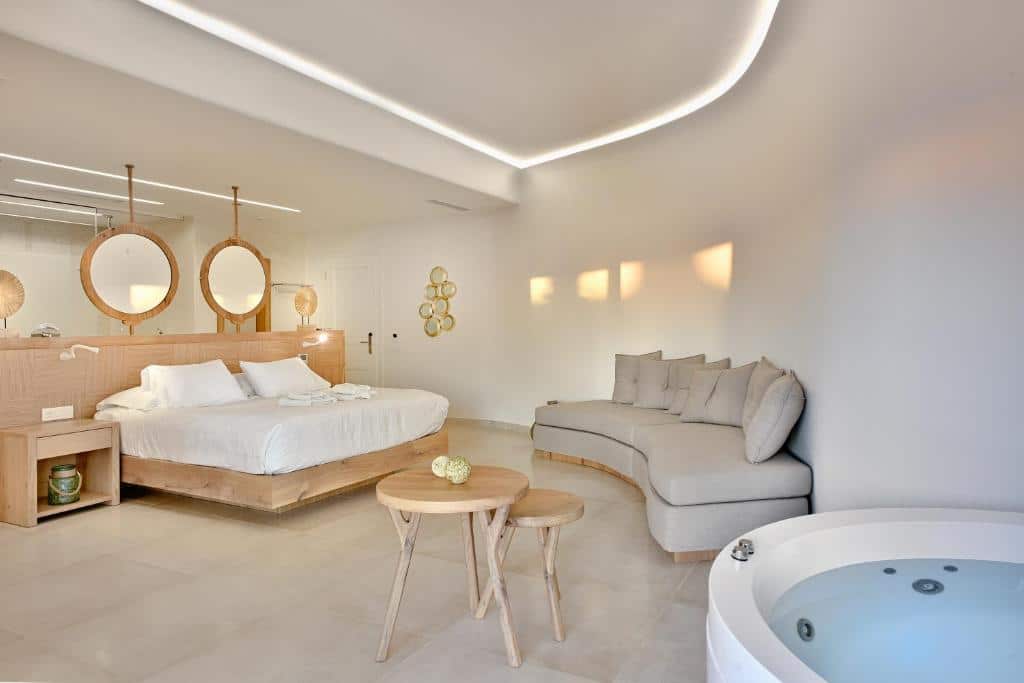 Quarto moderno do Anax Resort and Spa com uma cama grande, espelhos redondos, um sofá curvo, pequenas mesas e uma banheira de hidromassagem embutida, para representar hotéis em Mykonos.