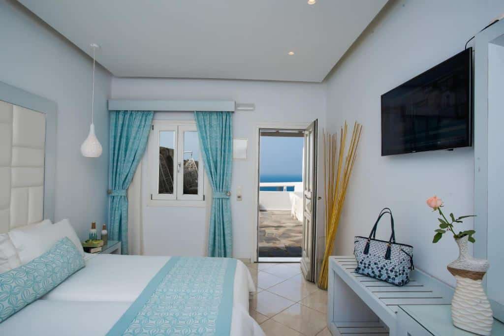 Um quarto bem arrumado no Damianos Mykonos Hotel, com paredes brancas, detalhes em azul, uma cama, uma TV e uma porta aberta com vista para o mar, para representar hotéis em Mykonos.
