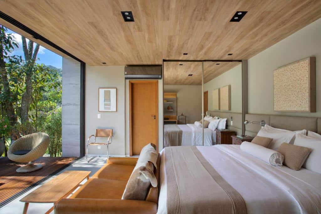 Quarto na Casa Marambaia Hotel com uma cama de casal, um armário com dois espelhos, um sofá de couro com dois lugares, na frente, há uma porta grande de vidro que leva para a varanda de conceito aberto, para representar hotéis em Petrópolis