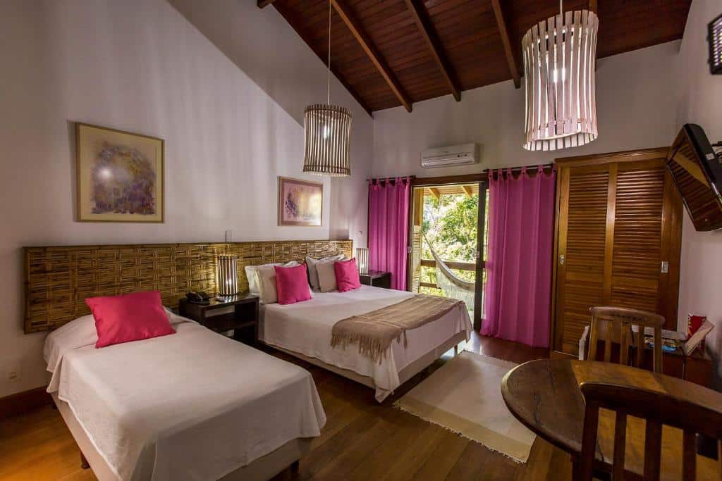 Quarto do Atelier Molinaro by Castelo Itaipava com uma cama de casal, uma de solteiro, uma varanda com rede de descanso, dois lustres rústicos, uma mesa com dois lugares e uma televisão 
