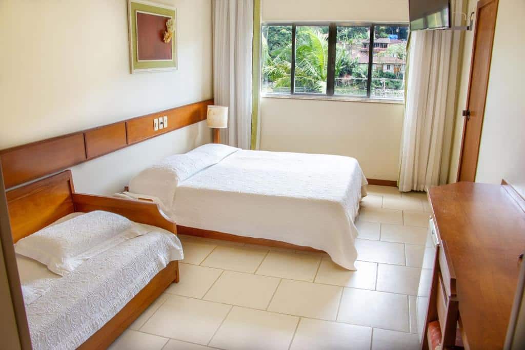 Quarto do Casa do Sol Hotel com uma janela com cortinas, televisão, uma cômoda com frigobar, uma cama de casal e uma de solteiro