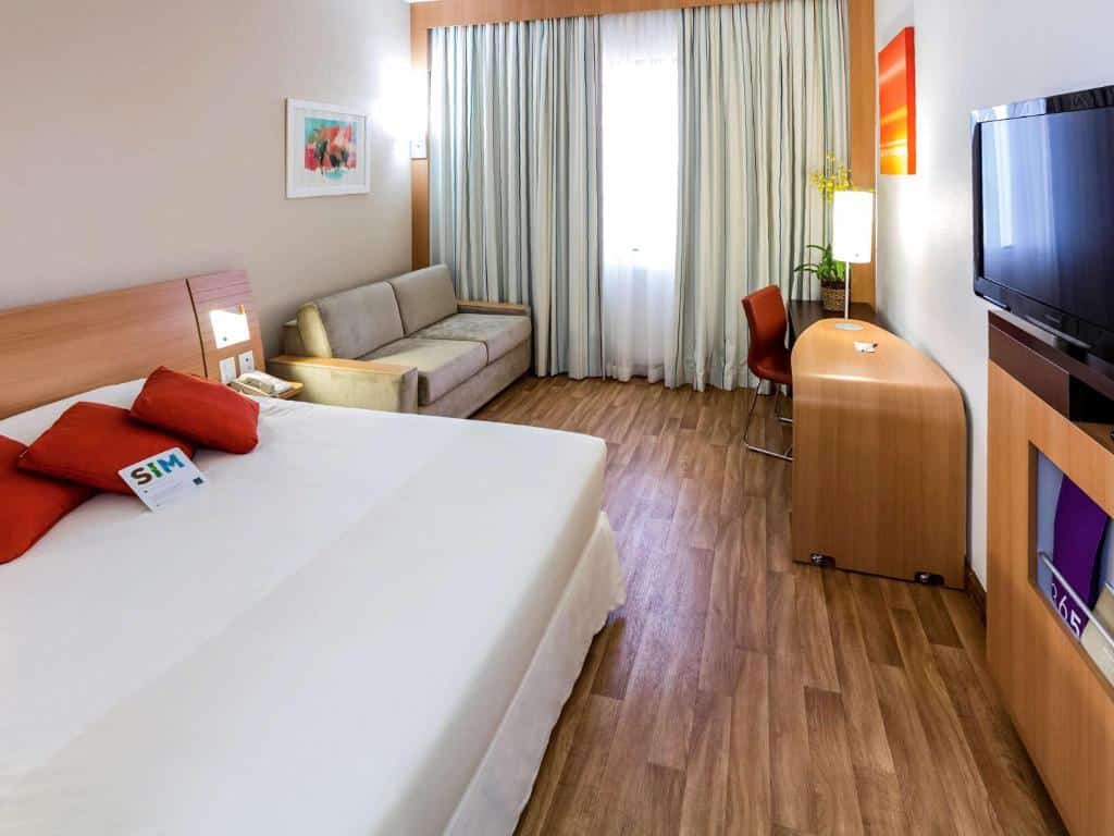 Quarto do Novotel Porto Alegre Três Figueiras, com TV, cama ampla, sofá-cama e mesa de trabalho