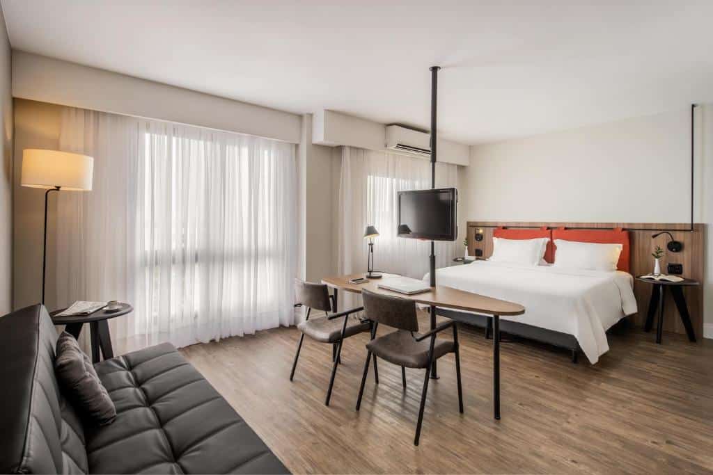 quarto de casal do Intercity Porto Alegre, com cama, TV giratória, mesa de trabalho, sofá e ar-condicionado