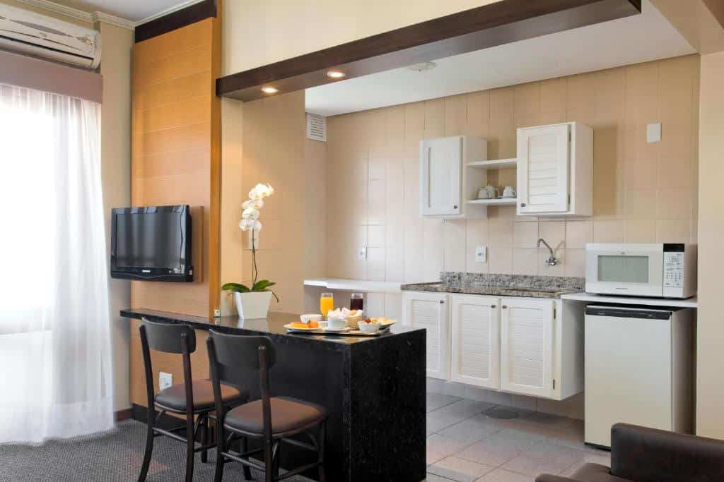 Quarto do Piazza Navona Porto Alegre by Intercity, um dos hotéis em Porto Alegre indicados, com mesa, TV, cadeiras, e uma área de cozinha com micro-ondas